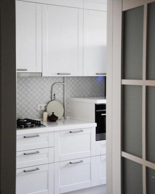 Меблировка обеденной зоны яркими цветными стульями в белом интерьере кухни.