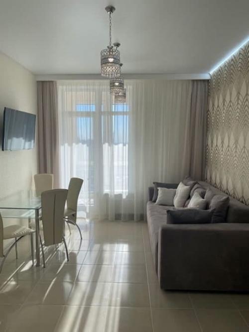 Объединенное пространство кухни - гостиной со столовой зоной в бежевых тонах с золотистыми элементами. 01